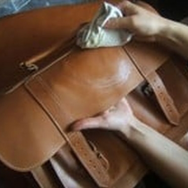 person rubbing oil onto a messenger bag with a cloth (Photo; Bidinis Handbags)