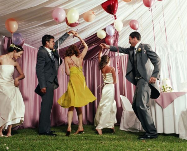 Two couples dancing at a wedding, with a single woman off to the left dancing by herself. (Photo: Getty Images)