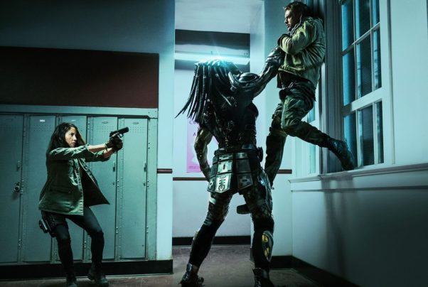 The Predator holding a man up in the air by his throat while Olivia Munn points a gun at the alien. (Photo: 20th Century Fox)