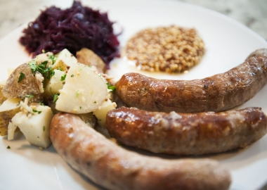 Three German sausages on a plate with German patato salad, rotessa sauerkraut and whole grain mustard. (Photo: Red's Table
