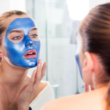 A woman applying a blue facial mask in mirror. (Photo: Jake Rosenberg)