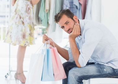 Man with shopping bag bored while woman searches clothes rack. (Photo: Shutterstock)