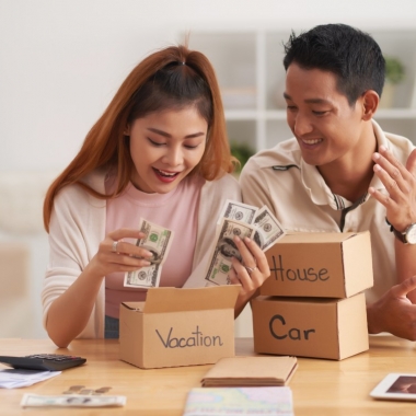 Young Asian couple putting money into boxes, saving for house, car and vacation. (Photo: Shutterstock)