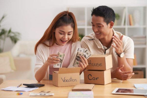 Young Asian couple putting money into boxes, saving for house, car and vacation. (Photo: Shutterstock)