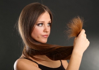 A woman holding split ends of her long hair, on black background. (Photo: Shutterstock)