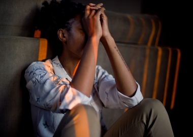 Stressed African American woman sitting on floor with knees up to chest, elbows resting on knees and hands against her forehead. (Photo: MasimbaTinasheMadondo/Pixabay)
