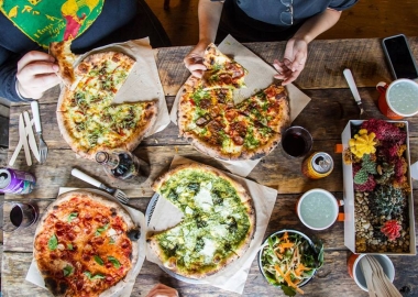 Diners sharing four different kinds of pizzas from Timber Pizza Co., which are on top of a wooden table. (Photo: Timber Pizza Co.)
