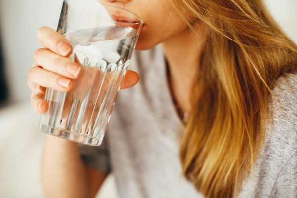 A woman drinking a tall glass of water. (Photo: Daria Shevtsova/Pexels)