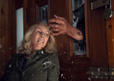 Jamie Lee Curtis leaning agains a door as a hand comes through the window in Halloween. (Photo: Universal Pictures)