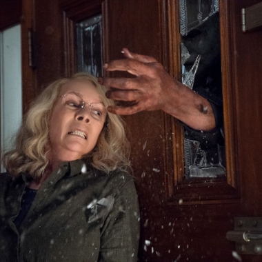 Jamie Lee Curtis leaning agains a door as a hand comes through the window in Halloween. (Photo: Universal Pictures)