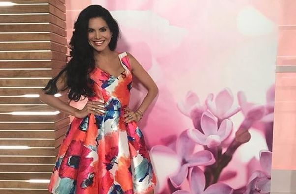 Joyce Giraud standing in a dress with orange and green poppies on it with her hands on her hips in front of a floral wall. (Photo: Joyce Giraud/Instagram)