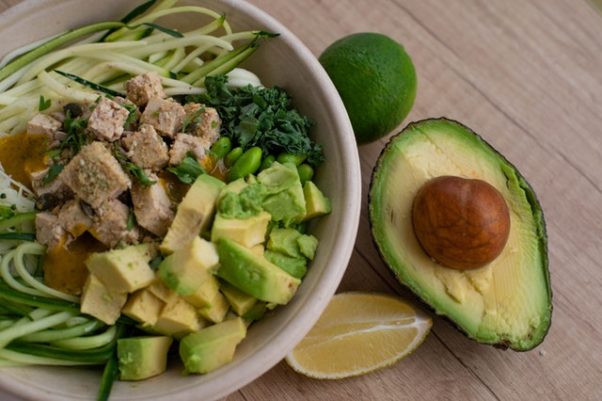 A bowl of salad with chicken, brocolli and avocado with a oime and half an avocado lying beside it. (Photo: Valeria Boltneva/Pexels)