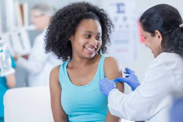 An African American woman in a blue tank top getting a shot from a female in a white lab coat. (Photo: iStock)