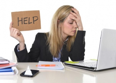 Woman sitting at computer with hand over face holding a sign that says help.