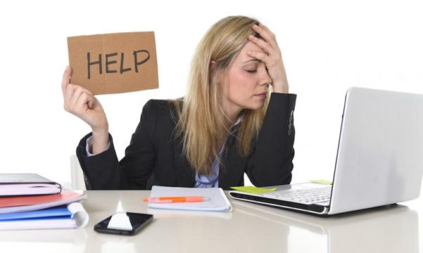 Woman sitting at computer with hand over face holding a sign that says help.