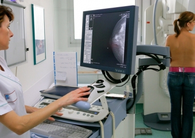 A closeup of a medical technicial at a monitor watching results of a far away woman getting a mammogram. (Photo: UIG via Getty Images)