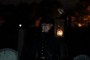 A tour guide carrying a lantern through grave stones. (Photo: Congressionl Cemetery)