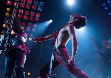 Freddy Mercury shirtless but wearing a tie performing on stage with the other members of Queen. (Photo: 20th Century Fox)