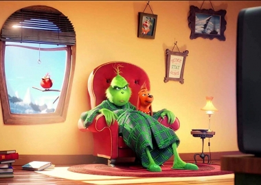 The Grinch sitting in a chair in his living room watching TV with Max the dog on his lap. (Photo: Universial Pictures)