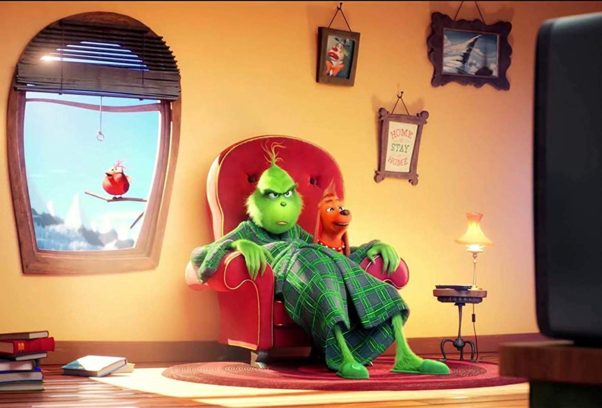 The Grinch sitting in a chair in his living room watching TV with Max the dog on his lap. (Photo: Universial Pictures)