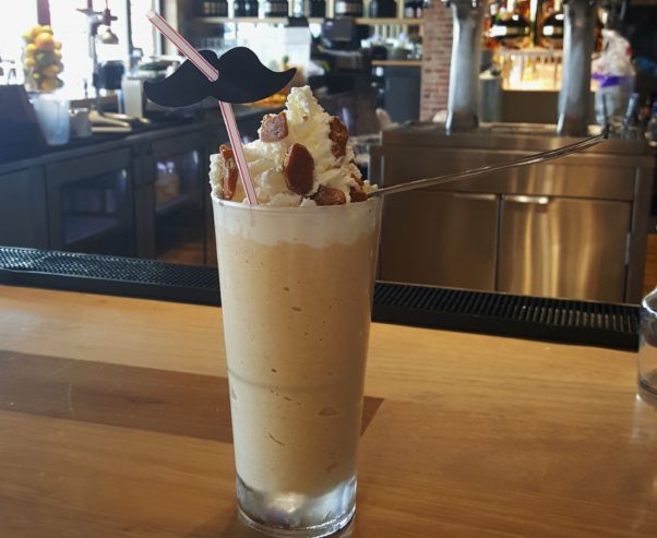 Pumpkin Stache milkshake sitting on a counter in on or the restaurants topped with whipped cream and pumpkin brittle with a stache straw. (Photo: Zinburger)