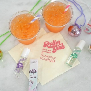 Bottles of Roller Girls Roll-On Lip Gloss scattered on a table among christmas ornaments and two orange socas with straws. (Photo: Honestyl Margo/Facebook)