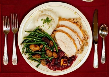 Plate of turkey cranberry sauce, green beans and mashed potatoes on a table with candles and saucer of gravy. (Photo: Getty Images)