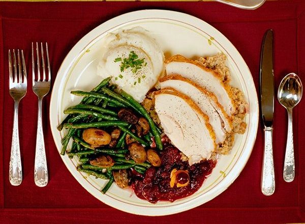 Plate of turkey cranberry sauce, green beans and mashed potatoes on a table with candles and saucer of gravy. (Photo: Getty Images)