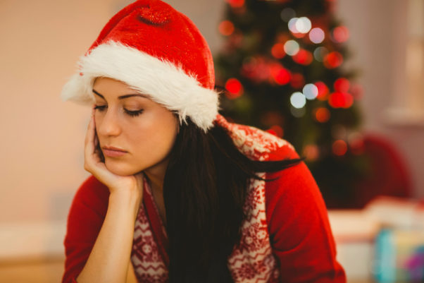 Depressed woman with chin on heand wearing red Christmas sweater and santa hat sitting in front of a Christmas tree. (Photo: 123rf)