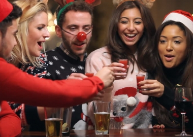Friends in Christmas sweaters, reindeer antlers, a red nose, etc. having a toast. (Photo: Shutterstock)