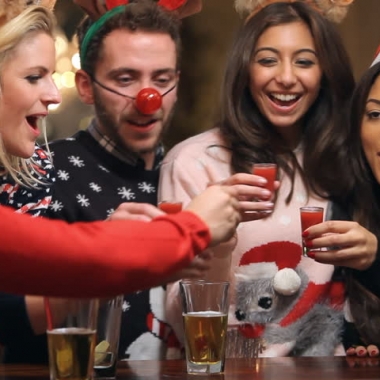 Friends in Christmas sweaters, reindeer antlers, a red nose, etc. having a toast. (Photo: Shutterstock)