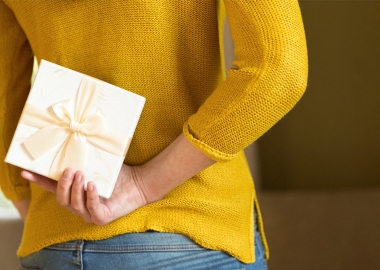 woman in yellow sweater in jeans hodling an envelope with a gift certificate in it behind her back. (Photo: Getty Images)