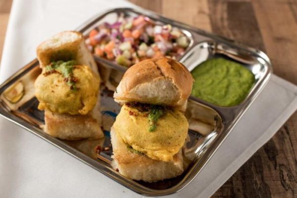 Two vada pavs on a metal tray with cilantro-ginger chutney and sauce. (Photo; Bombay Street Food)