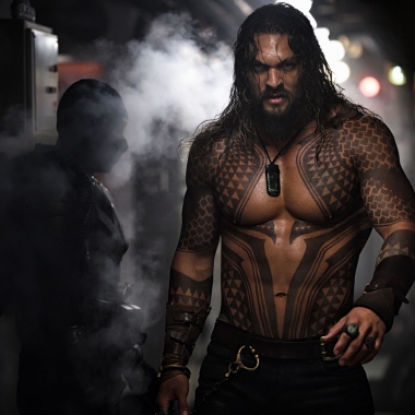 Actor Jason Momoa as a tattooed and shirtless Aquaman walks past another man in a submarine. (Photo: Warner Bros. Pictures)