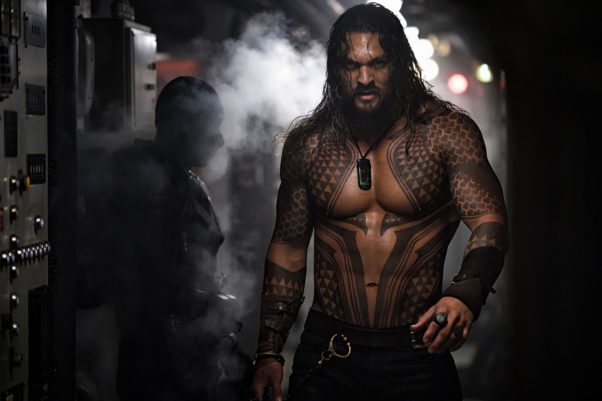 Actor Jason Momoa as a tattooed and shirtless Aquaman walks past another man in a submarine. (Photo: Warner Bros. Pictures)