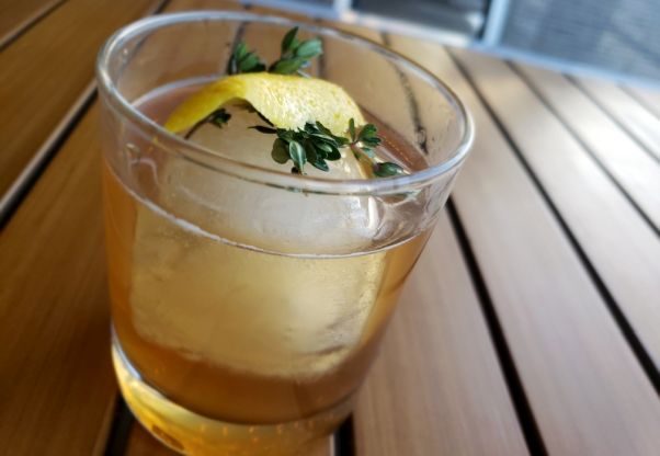 Red's Table's new Early Thyme winter cocktail in a highball glass with a large round ice cube and a lemon peel with fresh thyme. (Photo: Red's Table)