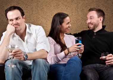 Three people sitting on a couch. Single man on left looks bored while woman and man have a fun conversation. (Photo: Shutterstock)