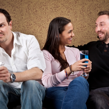 Three people sitting on a couch. Single man on left looks bored while woman and man have a fun conversation. (Photo: Shutterstock)