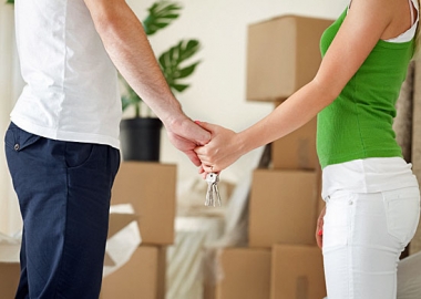 A man and woman holding hands and a set of keys with stacks of boxes and a plant in the background. (Photo: iStock Photo)