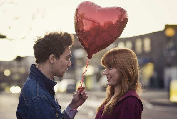 A man hainding a woman a heart-shaped balloon. (Photo: Getty Images)