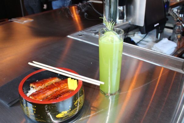 Broiled eel on top of rice in a black and red bowl with chopsticks and a green cocktails in a glass with somking rosemary. (Photo: Mark Heckathorn/DC on Heels)