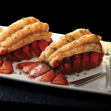Two lobster tails on a white rectangle plate with drawn butter on the left and lemon and a fork on the right. (Photo: Morton's)