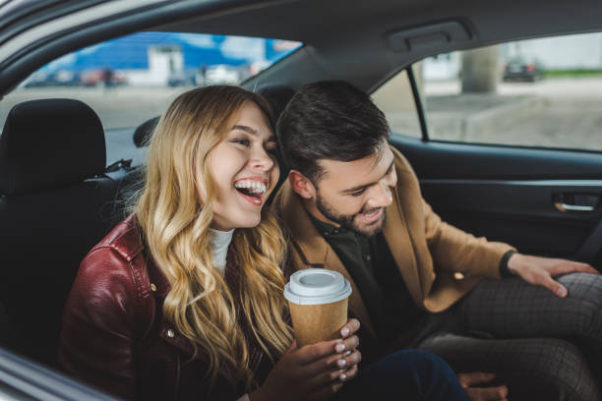 A happy young couple laughing while sitting together in taxi. (Photo: Shutterstock)