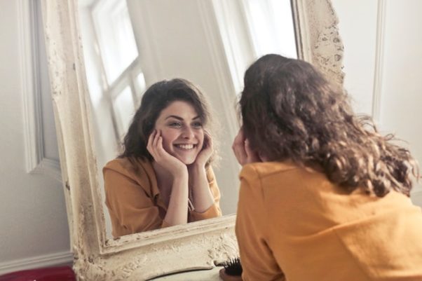 A woman smiliing into a mirror. (Photo: Bruce Mars/Pexels)