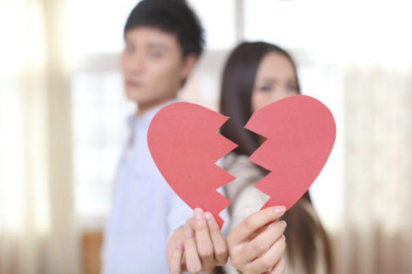 AnAsian couple out of focus in the background holidng a broken paper heart in the foreground. (Photo: iStock)