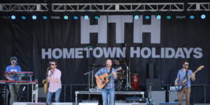 A band plays on a stage in front of a banner that says "HTH Hometown Holidays". (Photo: Hometown Holidays)