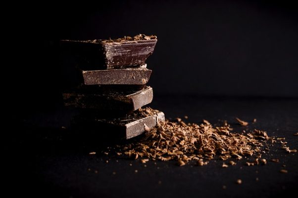 Four pieces of dark chocolate piled on top of each other beside chocolate shavings. (Phoot: StockSnap/Pixabay)