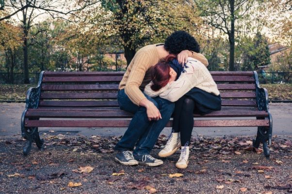 Man and woman on a park bench. Her with her head in her arms in his lap, him with his head in his arm on her back. (Photo: Shutterstock)
