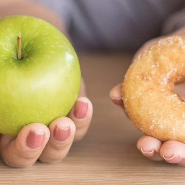 Woman's hands holding an apple and a glazed doughnut. (Photo: Getty Images)