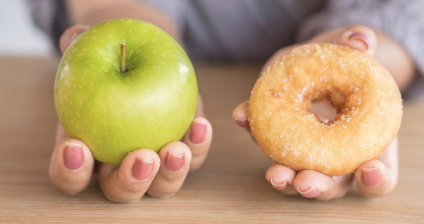 Woman's hands holding an apple and a glazed doughnut. (Photo: Getty Images)